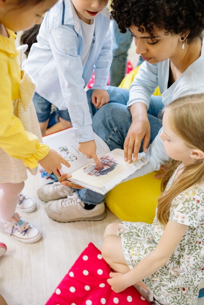 children-looking-at-a-book-holding-by-a-teacher-8613082 Preschool children gathered around a teacher reading a storybook indoors.